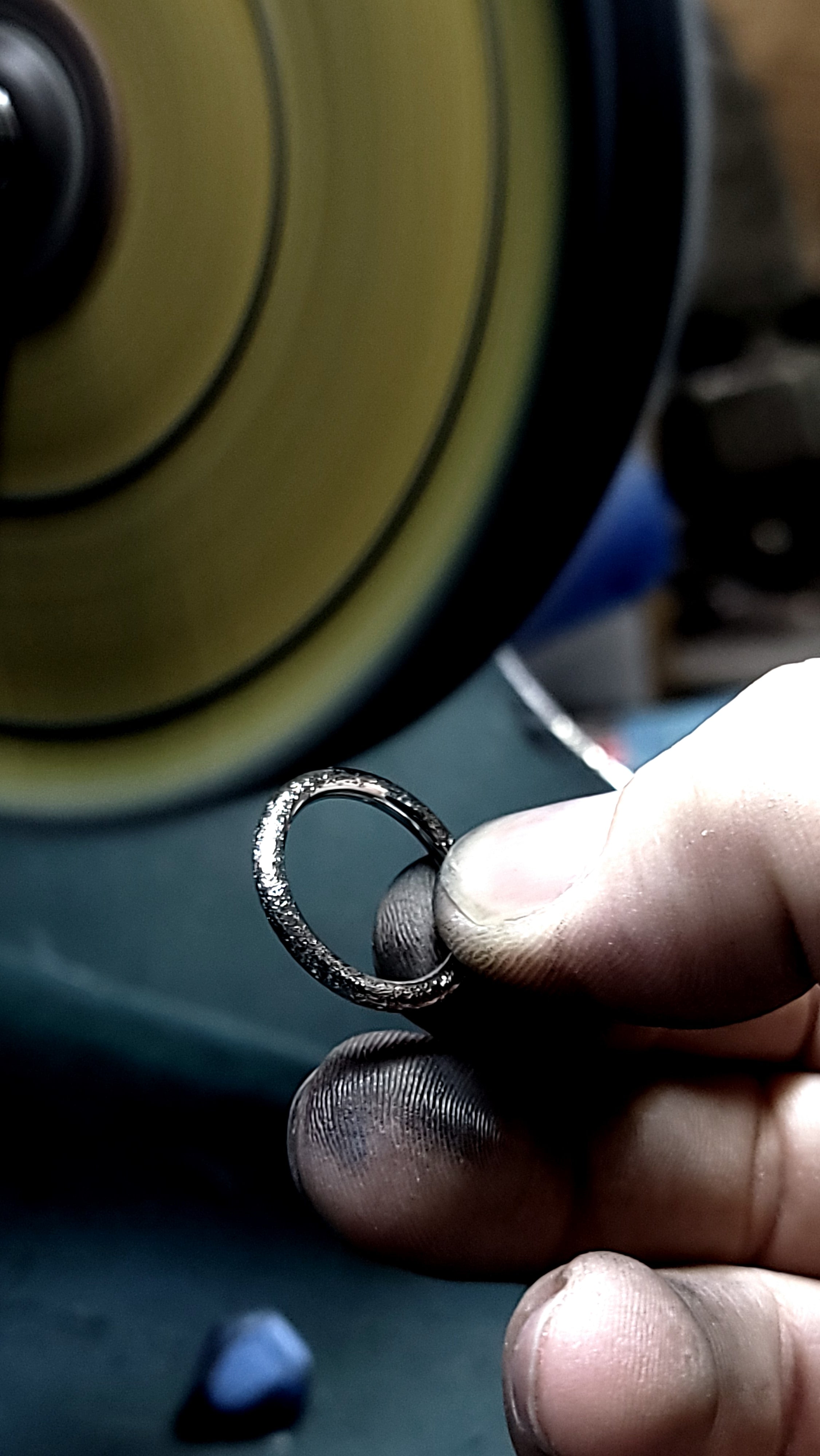 Hand holding a small metal ring near a polishing wheel