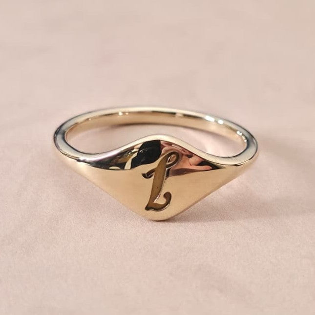 Gold cursive initial signet ring photographed for personalized jewelry trend showcasing 2026 fashion.