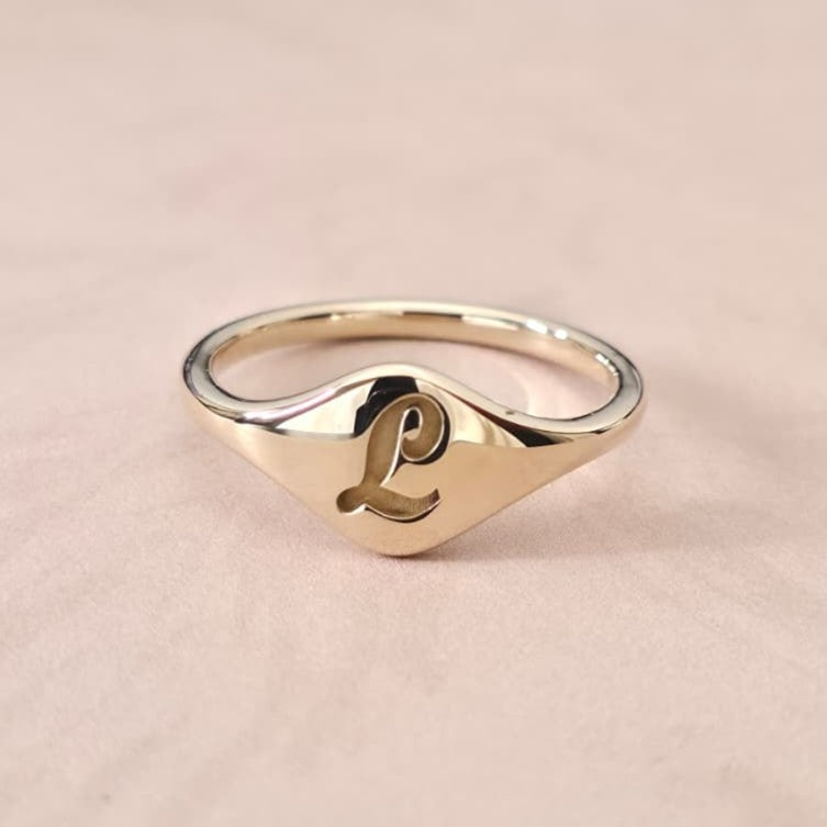 Gold cursive initial signet ring photographed to represent the modern evolution of historic signet rings.