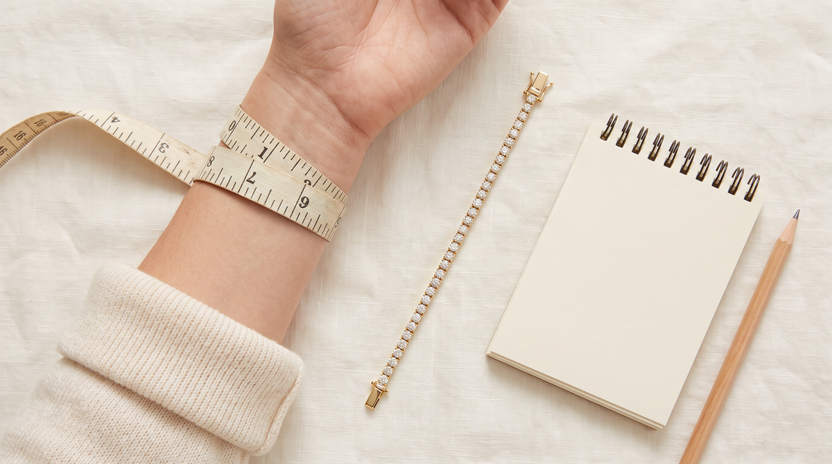 Measuring a wrist with a soft tape measure next to a gold diamond tennis bracelet