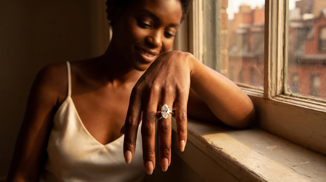 Close-up of a marquise Lab-Grown Diamond engagement ring in 14K yellow gold on a woman's hand resting on a sunlit windowsill