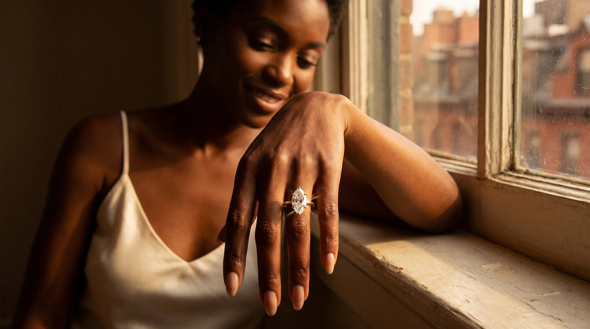 Close-up of a marquise Lab-Grown Diamond engagement ring in 14K yellow gold on a woman's hand resting on a sunlit windowsill