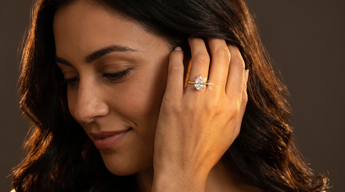 Close-up of a pear shaped Lab-Grown Diamond engagement ring in 14K yellow gold on a woman's hand tucking her hair behind her ear