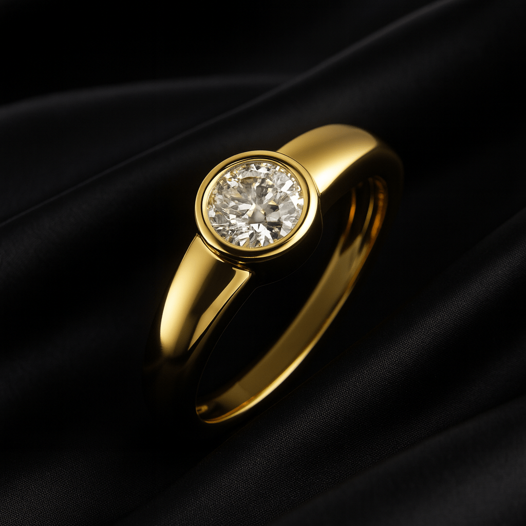 14K yellow gold bezel-set solitaire diamond ring displayed on black satin fabric, showcasing its modern minimal design and brilliant round-cut diamond.