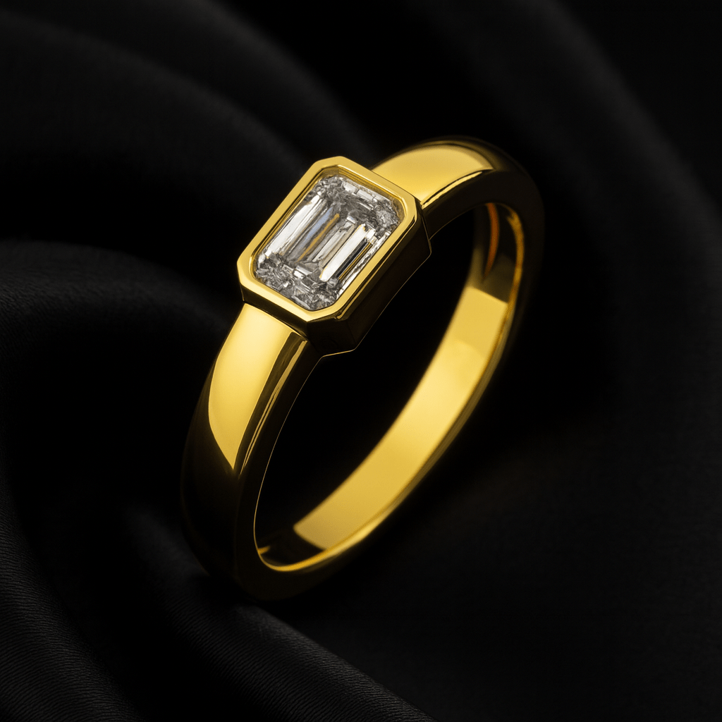 14K yellow gold emerald-cut bezel-set diamond ring displayed on black satin fabric, showcasing its modern geometric design and elongated step-cut facets.