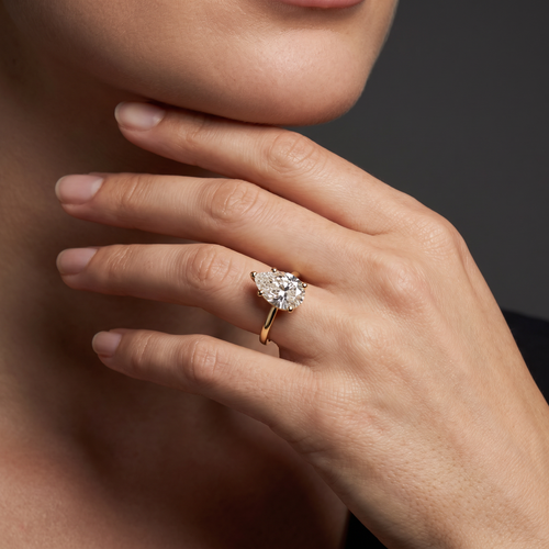 1.5ct pear cut diamond solitaire in 14K yellow gold worn on the hand, point facing the fingertip