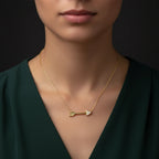 Close-up of 14K gold diamond arrow necklace on model wearing deep green silk top, Black Pearl of Queens fine jewelry