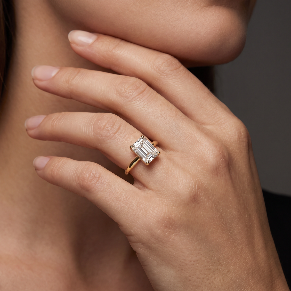1ct emerald cut solitaire engagement ring in 14K yellow gold worn on hand, step-cut table facing up