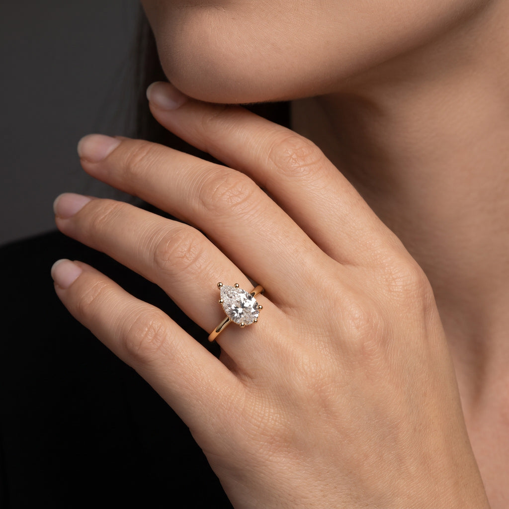 Hand wearing a 2 carat pear shaped Lab-Grown Diamond hidden halo engagement ring in 14K yellow gold
