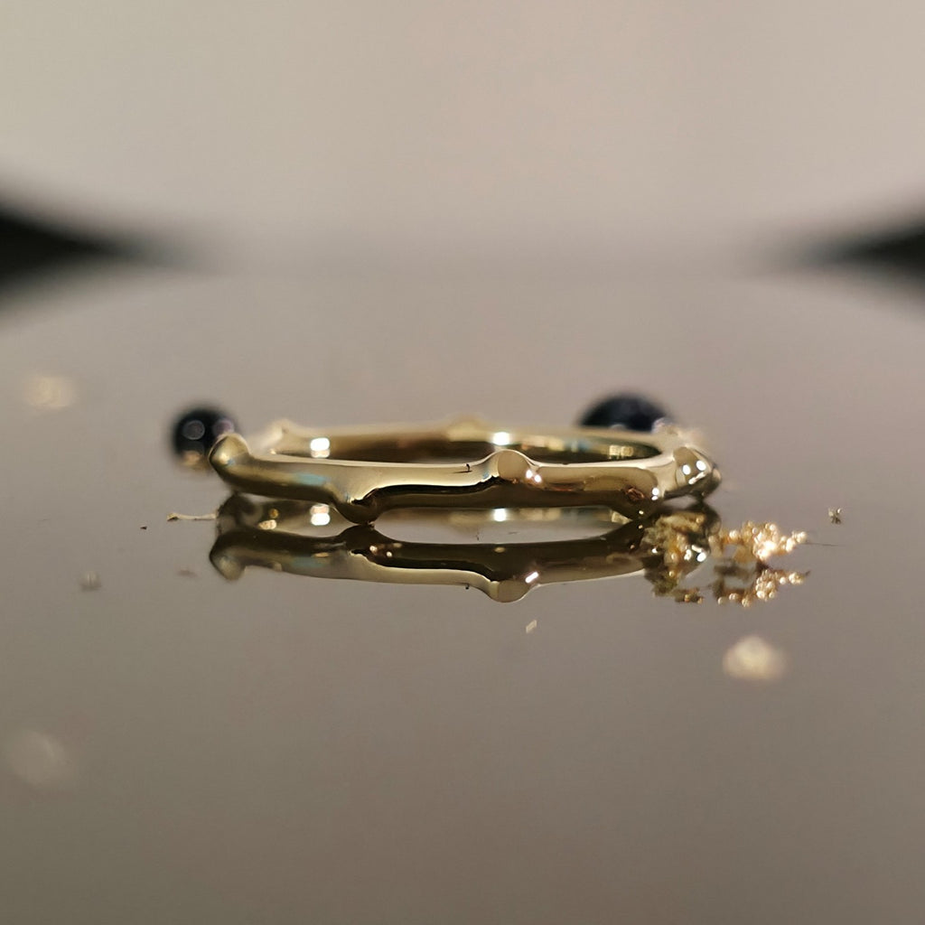 Organic bamboo-inspired gold ring on reflective surface, minimalist wedding band design