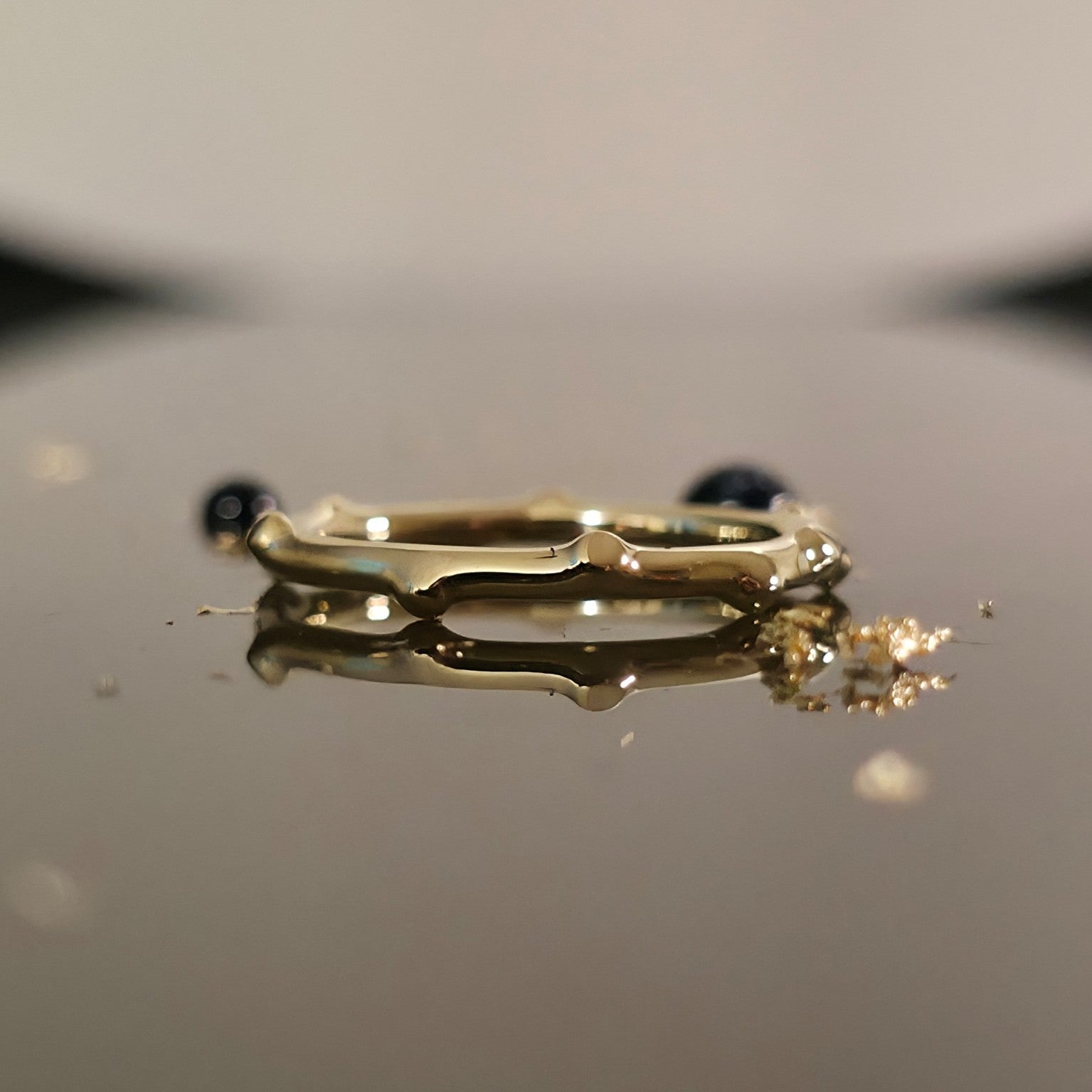 Organic bamboo-inspired gold ring on reflective surface, minimalist wedding band design