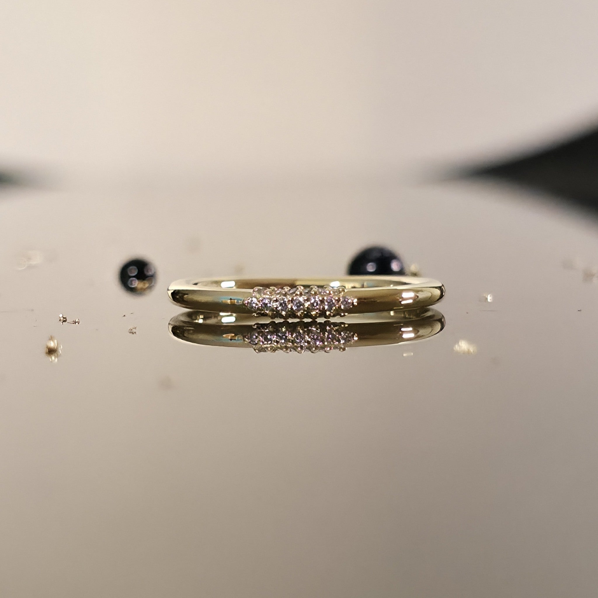 Diamond wire ring in 14K yellow gold with petite cluster of diamonds, slim 2mm wire wedding ring close-up on reflective surface