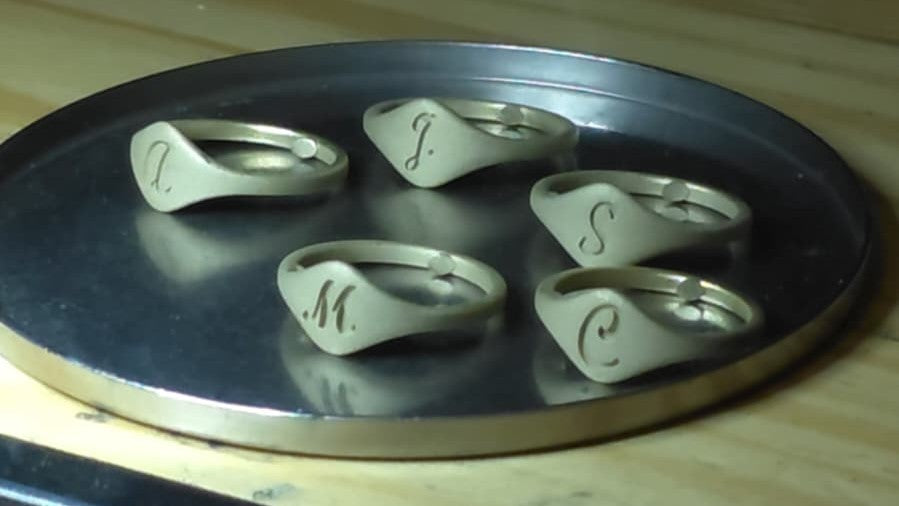 Raw cast gold initial signet rings before polishing, displayed on a jeweler’s bench to show the hand-crafted production process.