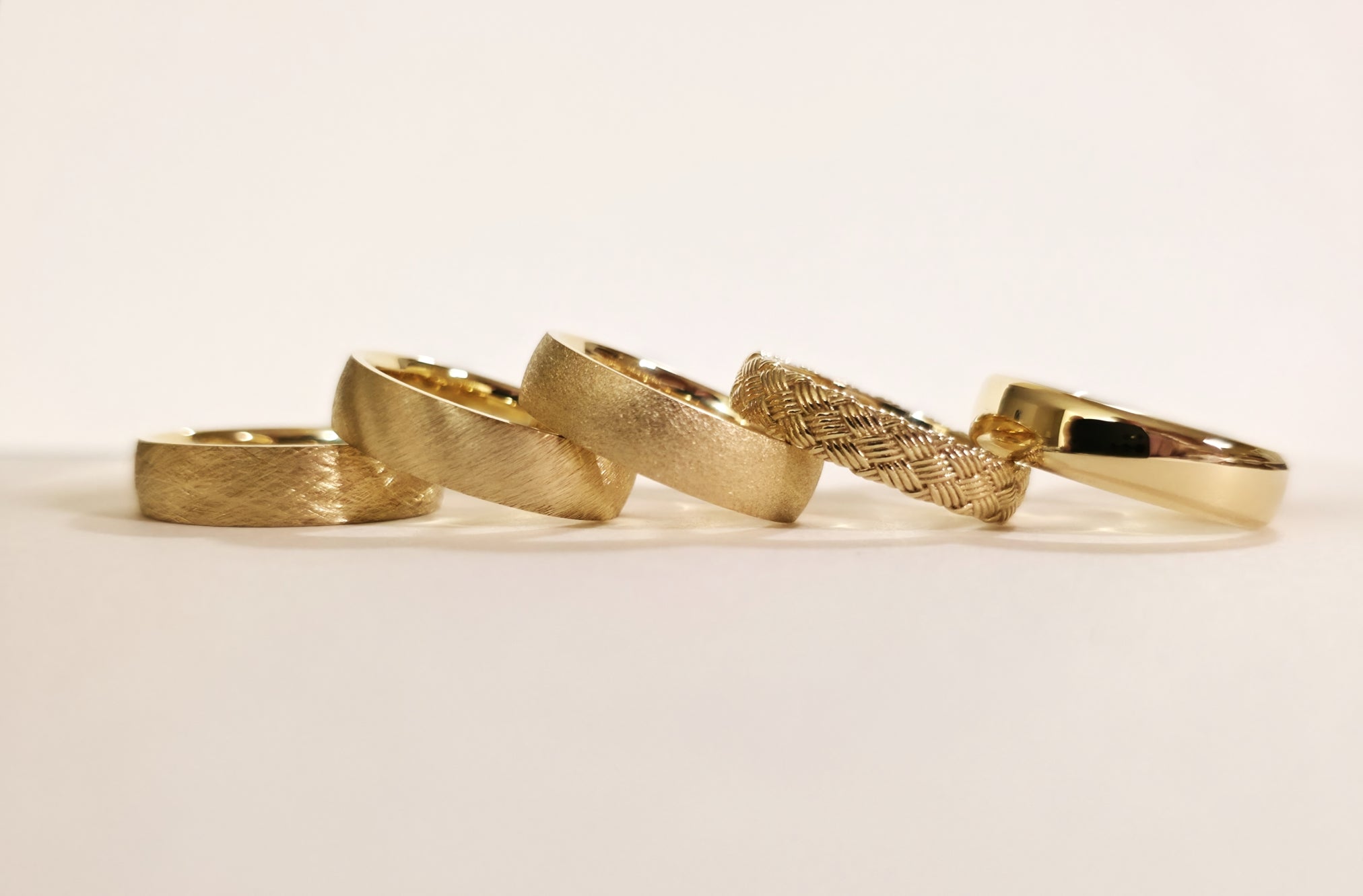 Five gold rings of different designs on a light beige background