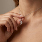Model holding Aurex Capricorn Zodiac Diamond Necklace in 14K white gold between fingers at décolletage, close-up editorial shot showing full pendant detail