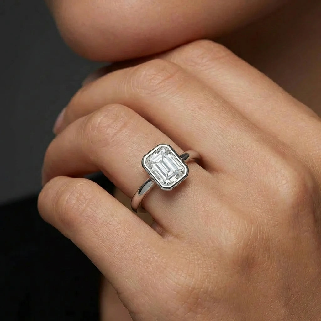 Model wearing emerald cut diamond ring in solid gold with bezel setting and modern minimalist design
