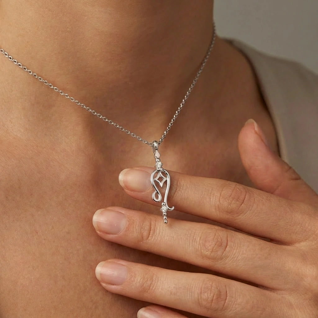 Model holding Aurex Leo Zodiac Diamond Necklace in 14K white gold between fingers at décolletage, close-up editorial shot showing open Leo glyph with star cutout and twin diamonds