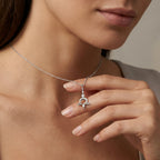 Model holding Aurex Libra Zodiac Diamond Necklace in 14K white gold between fingers at décolletage, close-up editorial shot showing Libra scales symbol with twin diamonds