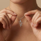 Model holding Aurex Virgo Zodiac Diamond Necklace in 14K white gold between fingers at décolletage, close-up editorial shot showing script-like Virgo glyph with bezel-set diamond crown