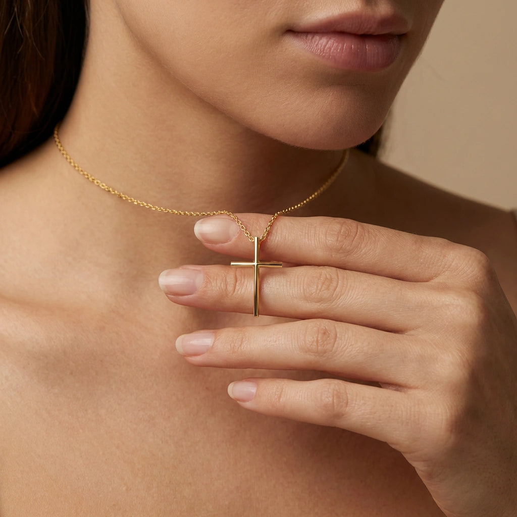 Close-up of 14K yellow gold Axis minimal cross necklace worn on model holding pendant with hand