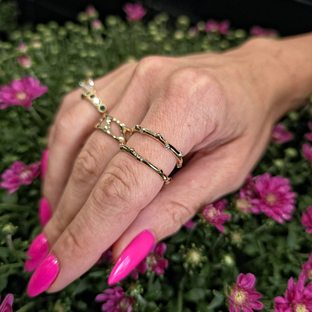 Hand wearing organic bamboo gold ring with pink nails and flowers in background
