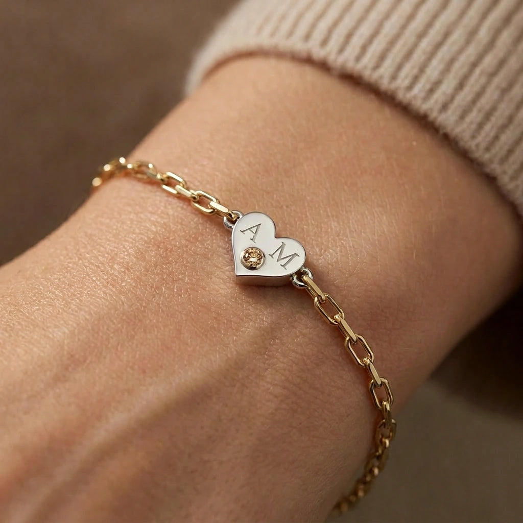 Brownstone champagne diamond heart bracelet with engraved initials worn on wrist — 14K white gold heart charm on yellow gold paper clip chain, close-up lifestyle view