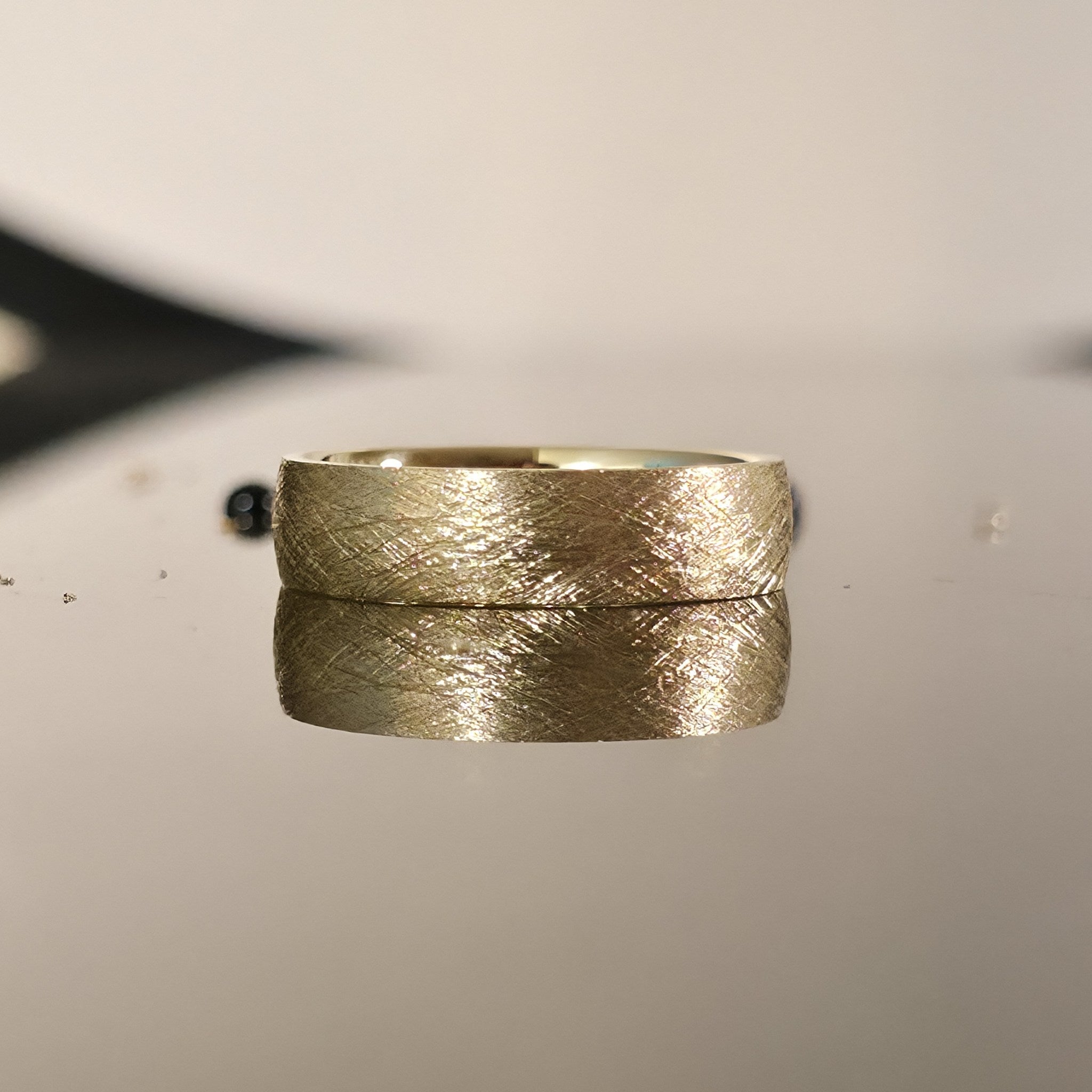 Close-up of brushed gold wedding band with matte finish, 14K 6mm handcrafted ring reflection photo
