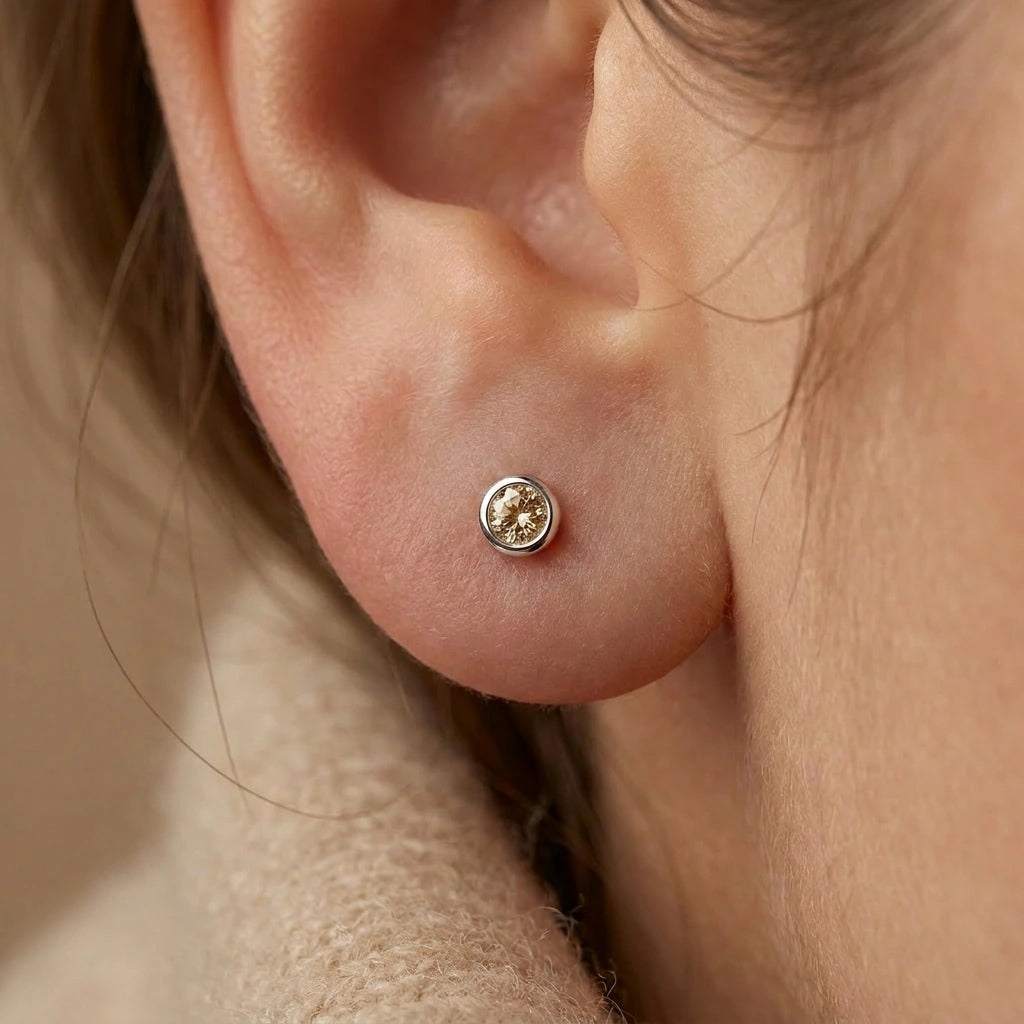 Champagne diamond bezel stud earrings in 14K yellow gold worn in helix and lobe — stacked ear styling