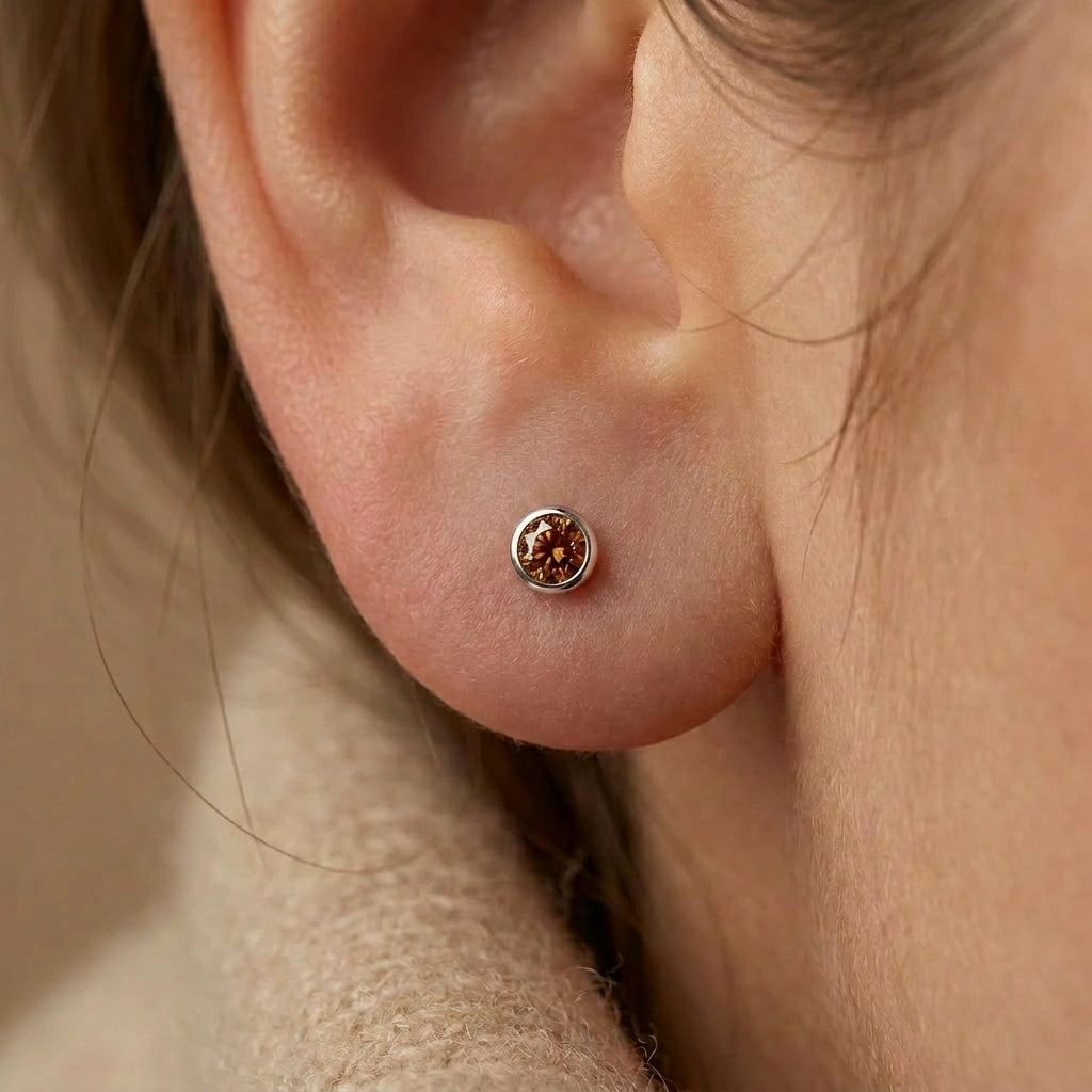 Cognac diamond bezel stud earring in 14K white gold worn on ear — close-up lifestyle view