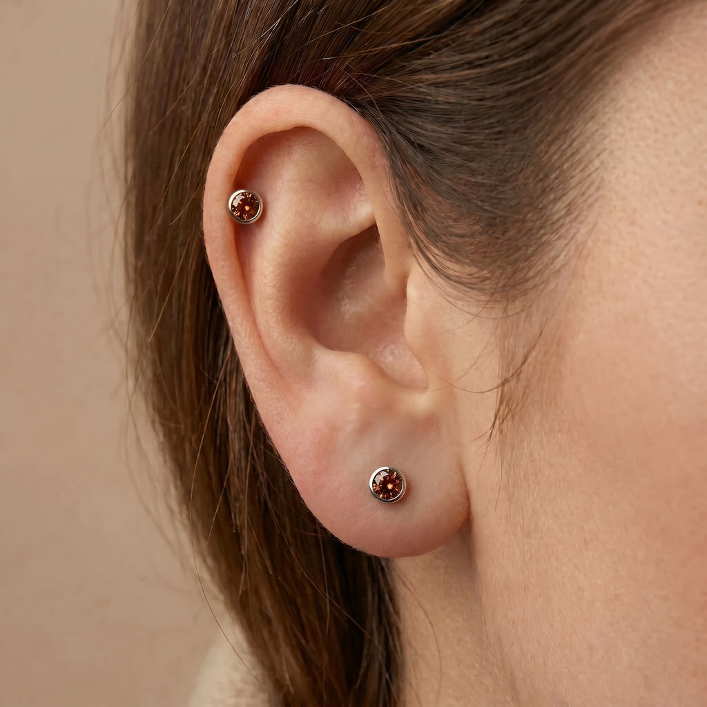 Cognac diamond bezel stud earrings in 14K white gold worn in helix and lobe — stacked ear styling