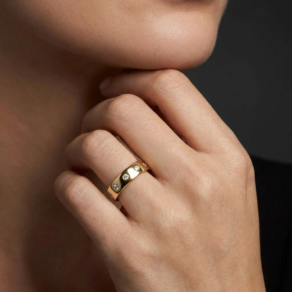 Female model wearing Cyrus Diamond Station Band in 14K yellow gold, close-up editorial portrait showing wide domed band with 12 flush bezel-set D-F colorless lab diamonds scattered around circumference