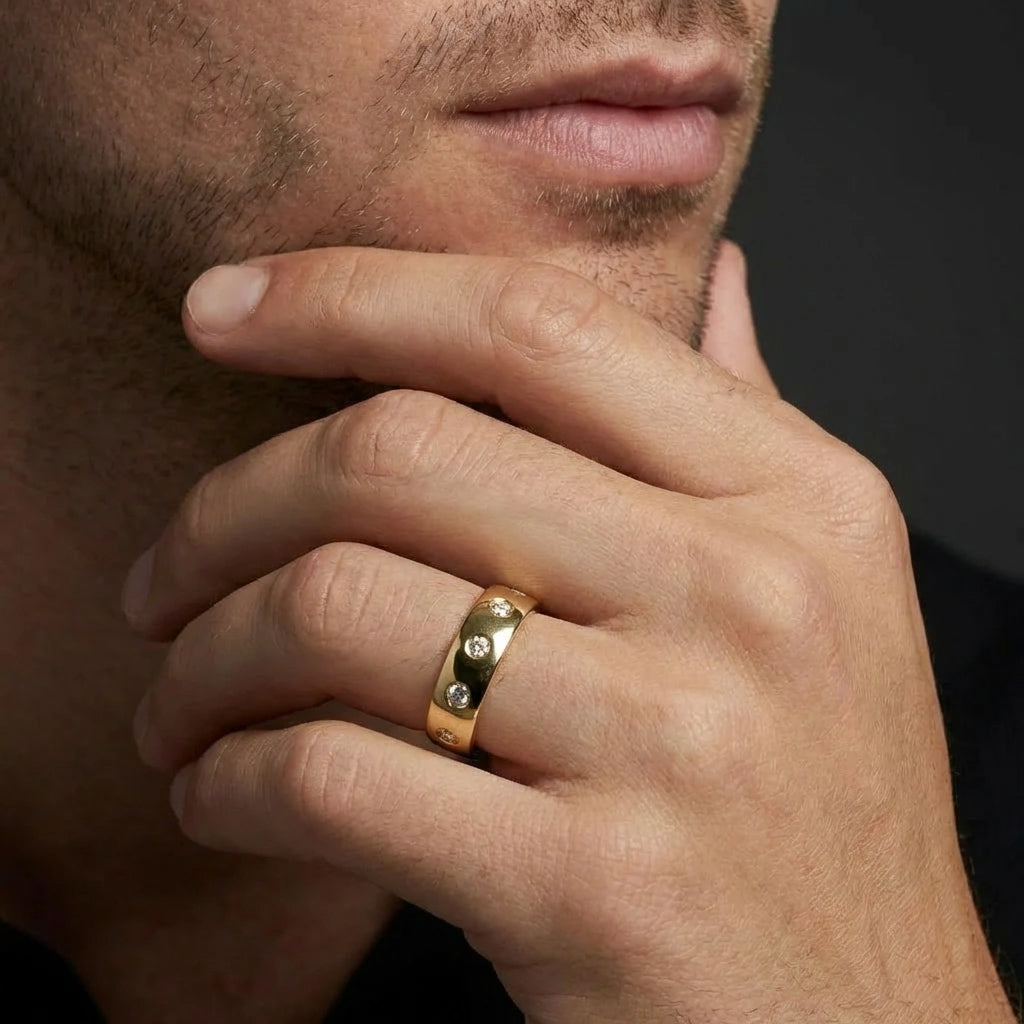 Male model wearing Cyrus Diamond Station Band in 14K yellow gold, close-up editorial portrait showing wide domed band with 12 flush bezel-set D-F colorless lab diamonds scattered around circumference