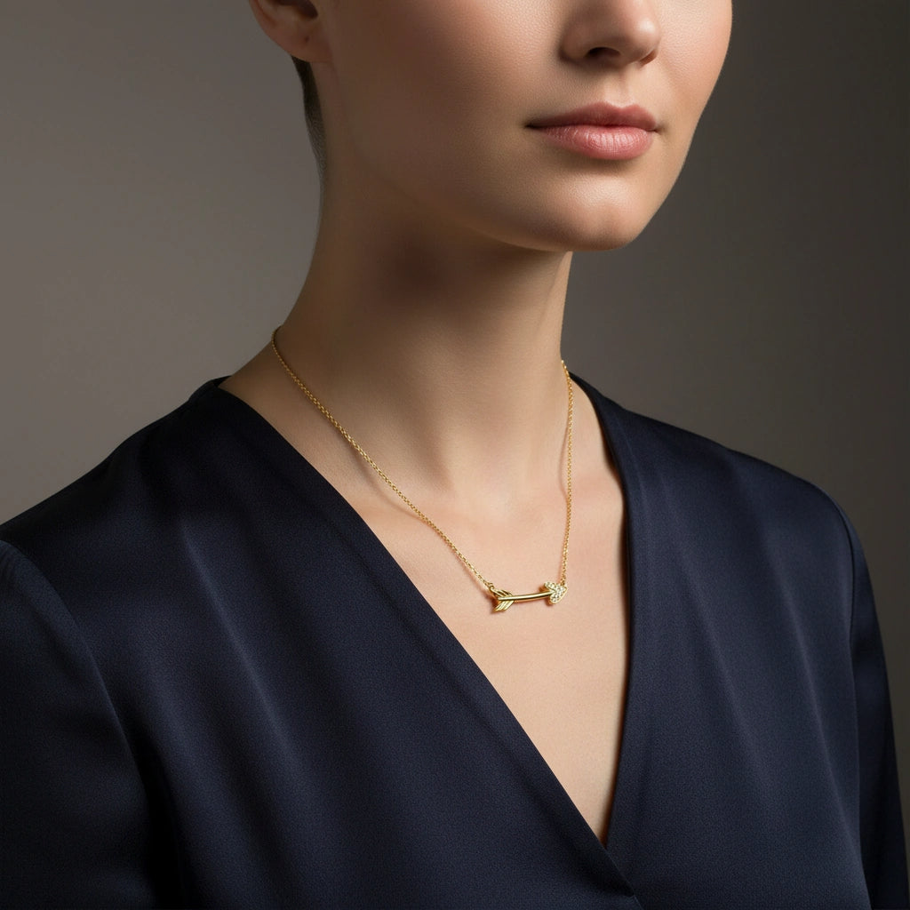 Woman wearing a 14K solid yellow gold diamond arrow necklace styled with deep navy silk blouse in luxury studio setting