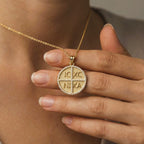 Close-up of woman holding 14K gold engraved cross medallion necklace with diamond pavé border