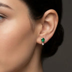 Woman wearing Elyra emerald drop stud earrings with pear shaped green gemstone and diamond detail