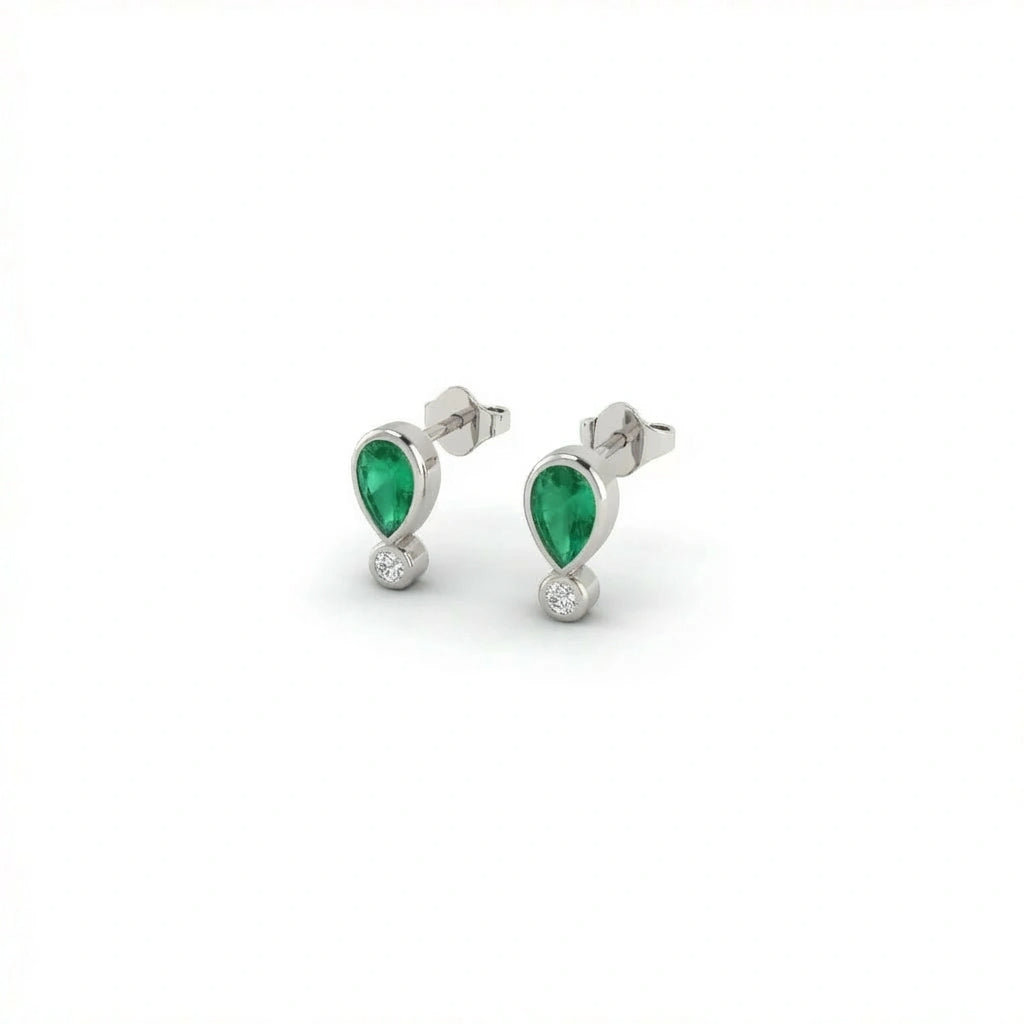 Elyra emerald drop stud earrings in solid white gold featuring pear shaped green gemstone with round diamond accent