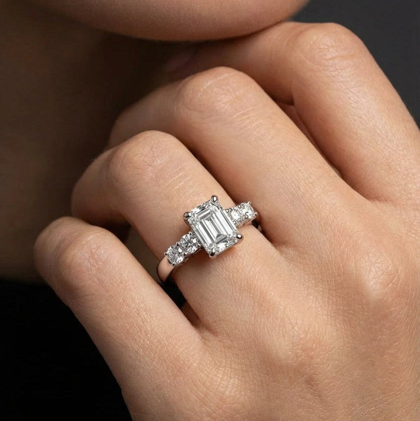 Emerald cut five-stone engagement ring worn on hand, 1ct center with round side stones across the finger