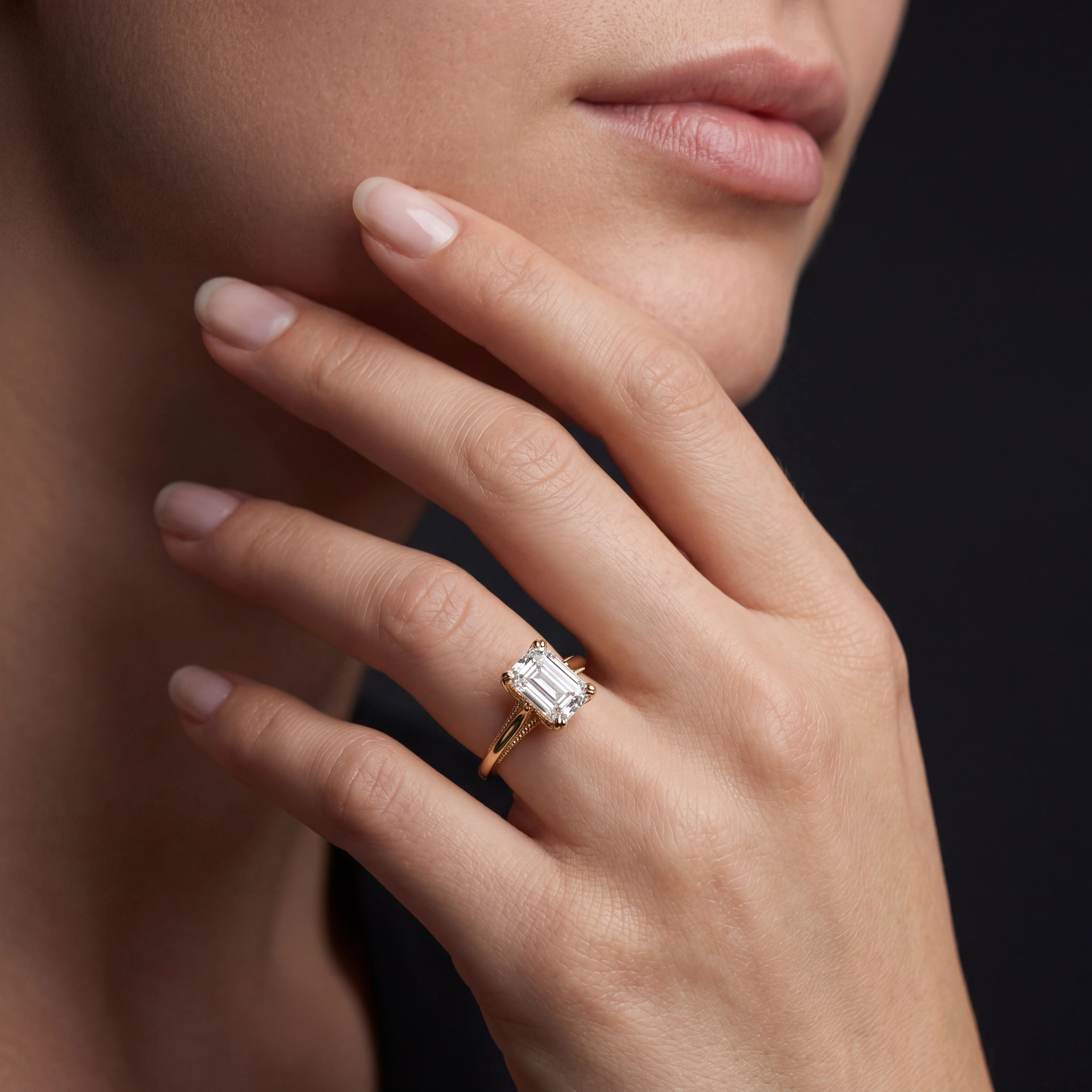 Model wearing emerald cut lotus prong milgrain Lab-Grown Diamond engagement ring in 14K yellow gold, close-up showing petal prong setting and gallery detail — Black Pearl of Queens