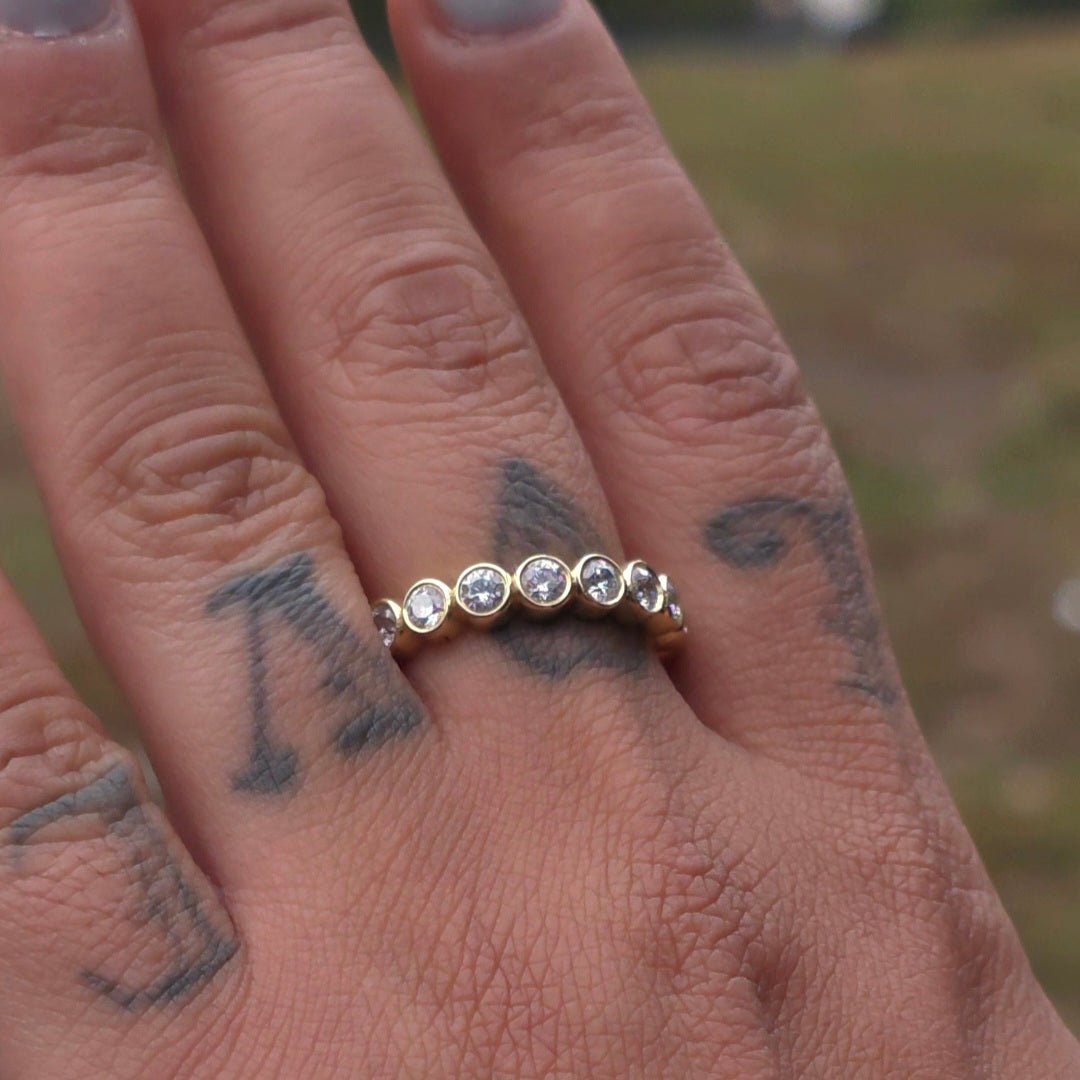 Close-up of a hand wearing a gold ring with diamonds on a blurred natural background