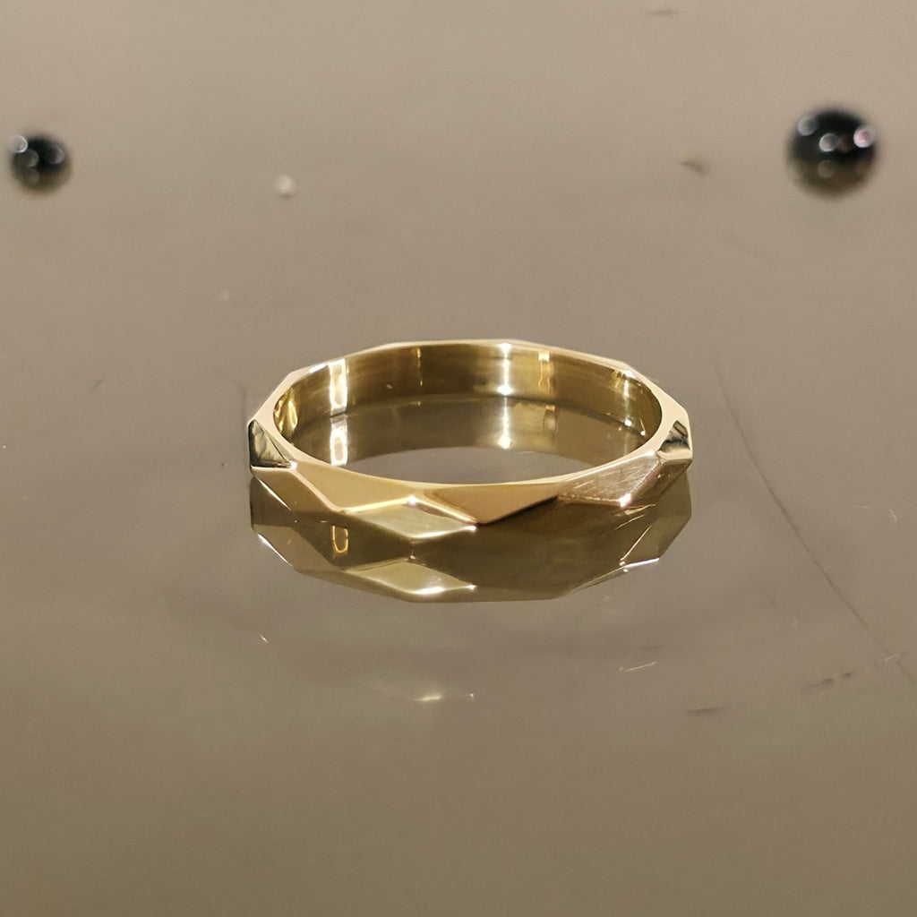 Close-up of 3mm faceted solid gold ring on reflective surface
