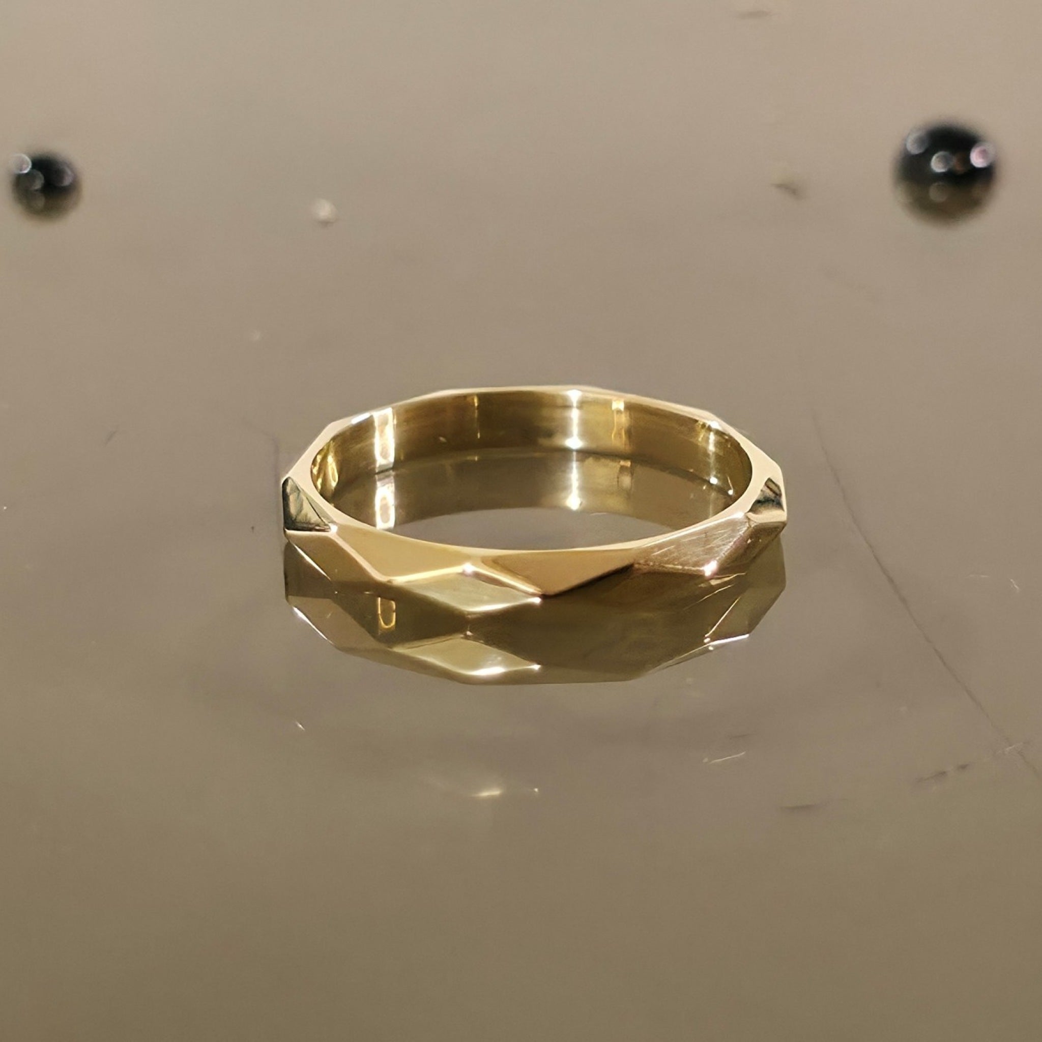 Close-up of 3mm faceted solid gold ring on reflective surface