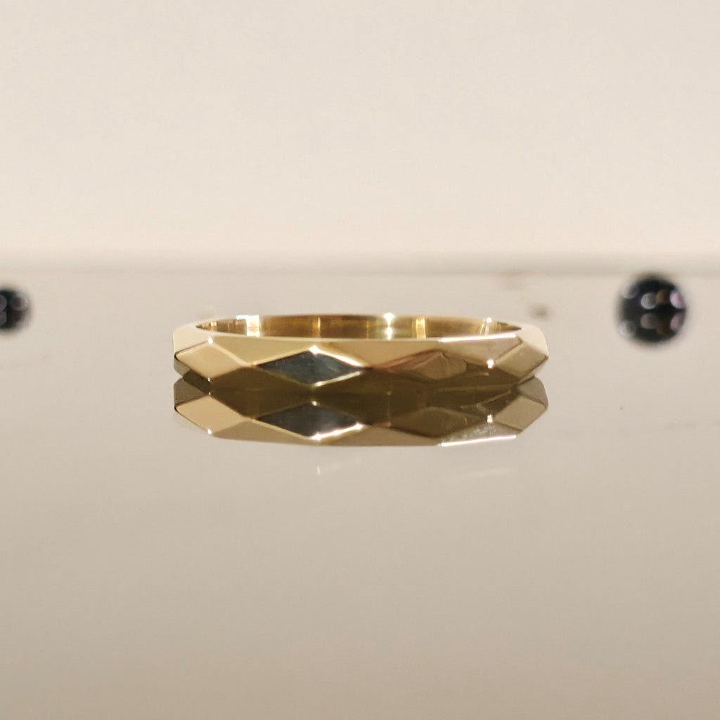 3mm faceted gold ring reflecting on a mirror surface