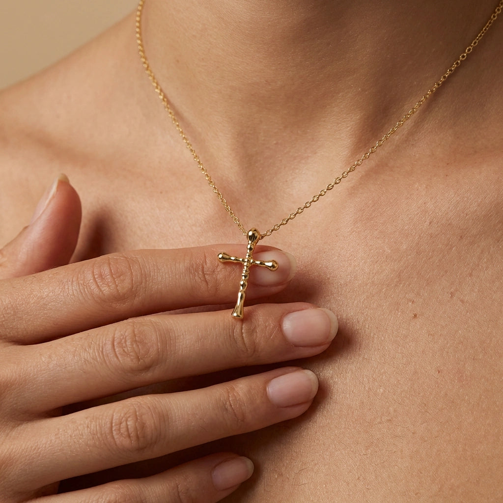 Close-up of woman holding 14K gold Faithline cross necklace at collarbone showing small beveled pendant design