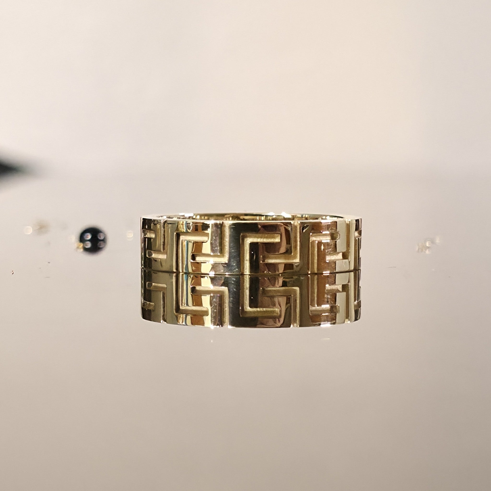 Close-up of solid gold Greek key ring with meander design on reflective surface