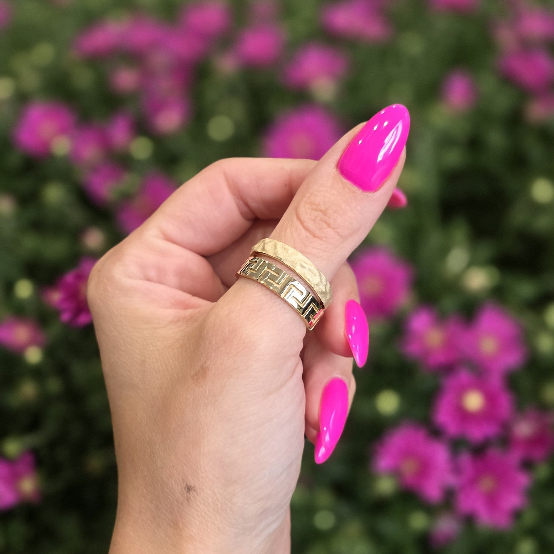 Greek key ring in solid gold worn on thumb with pink nails, floral background