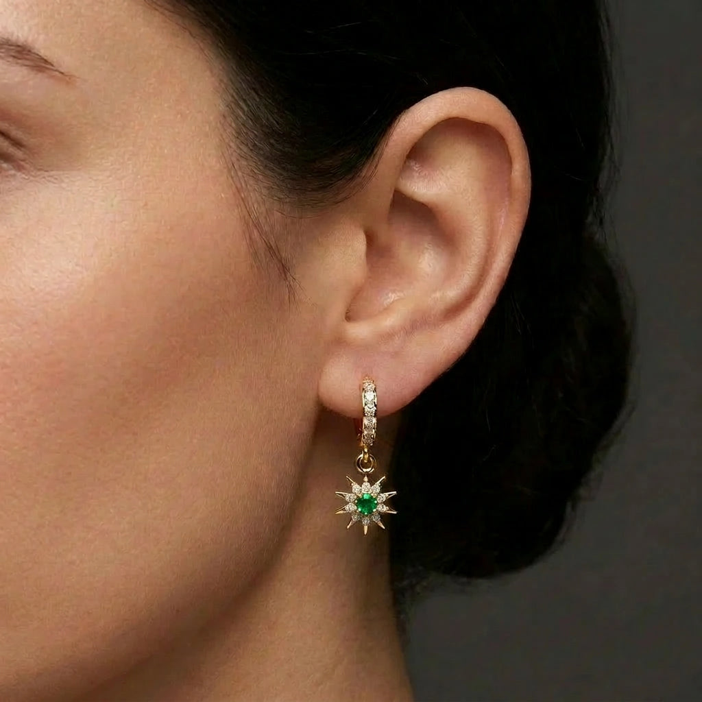 Woman wearing Helion emerald starburst hoop earrings with radiant drop design and green center stone