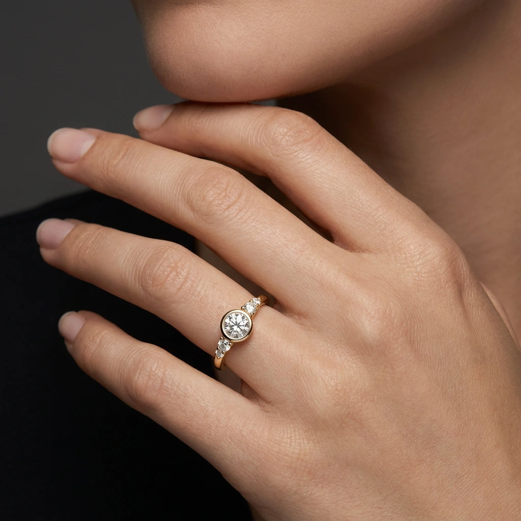 Lab-grown diamond bezel engagement ring on hand in 14K yellow gold, dark background