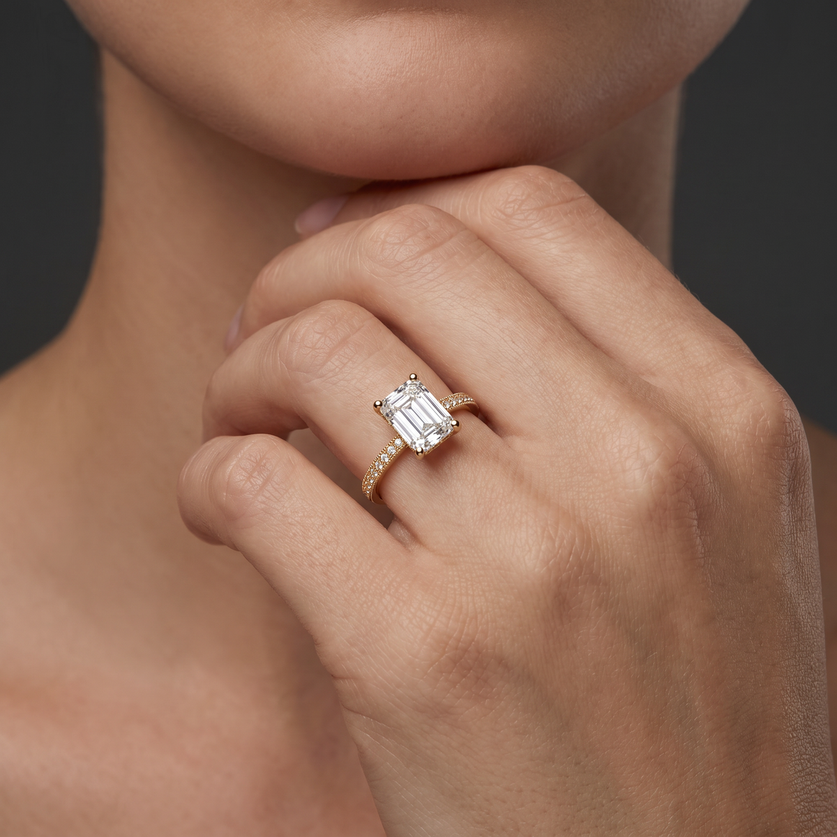 Hand wearing an emerald cut Lab-Grown Diamond milgrain pavé engagement ring in 14K yellow gold