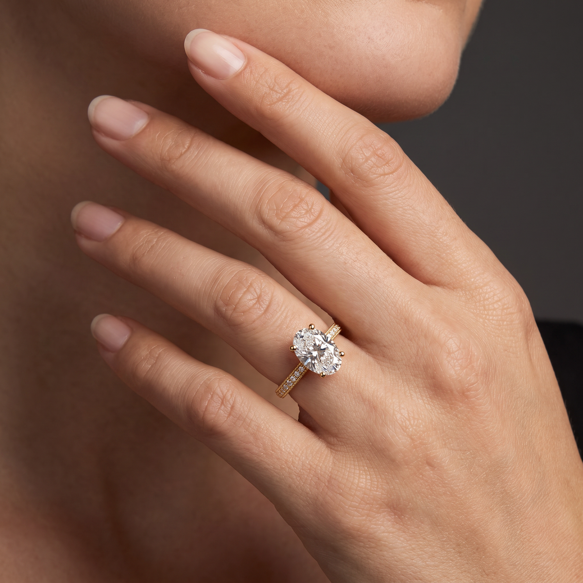 Hand wearing an oval Lab-Grown Diamond milgrain pavé engagement ring in 14K yellow gold