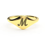 M initial cursive signet ring in polished 14K gold on a soft beige background.